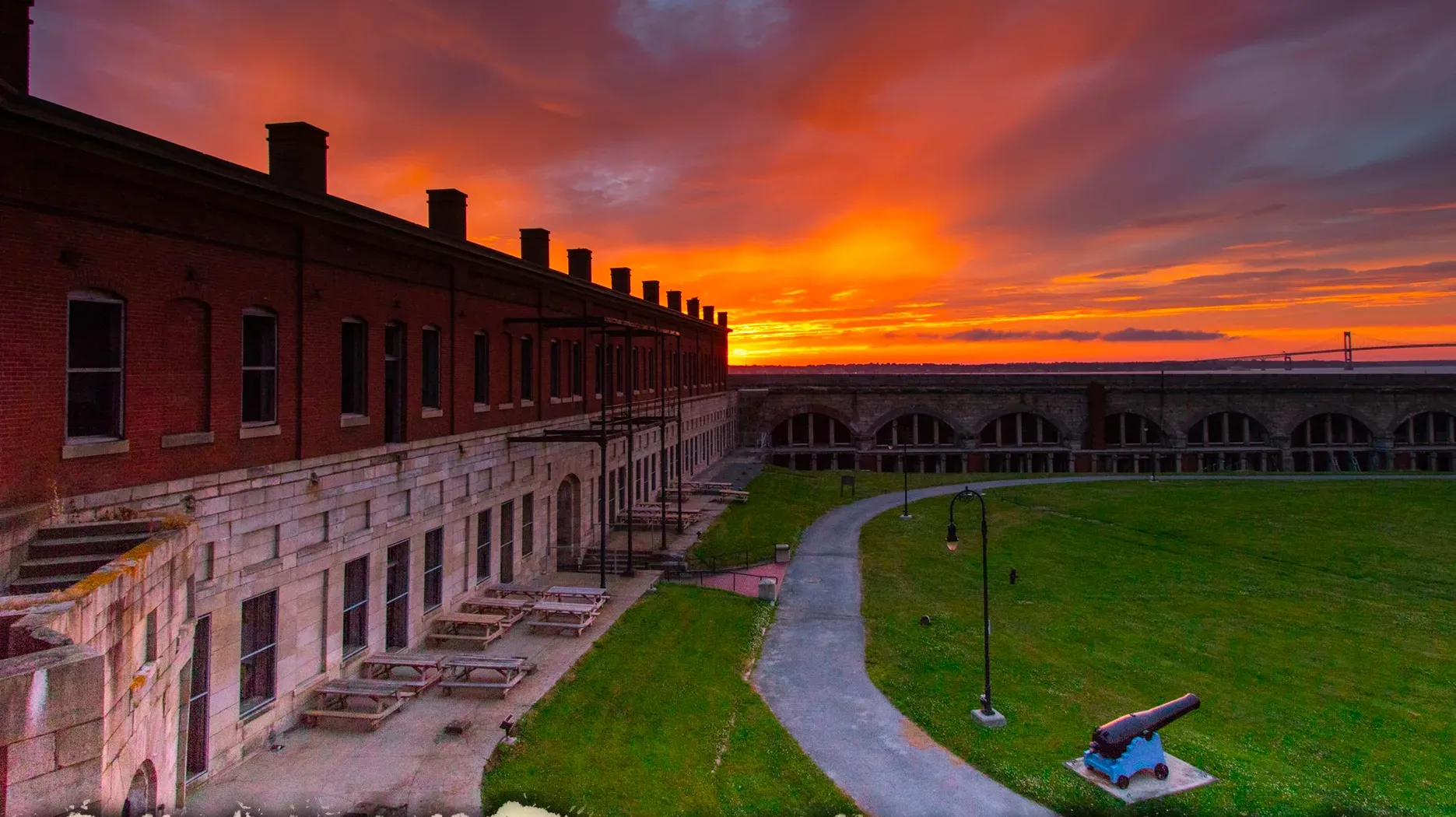 Sunset over the parade field at Fort Adams, with a cannon on the lawn and the arched casemates beyond